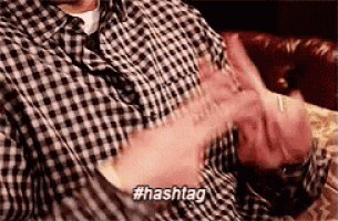a man in a plaid shirt is sitting on a couch with his hands in the air .