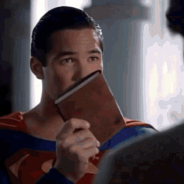 a man in a superman costume holds a book in front of his face