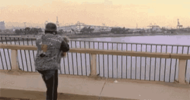a man is standing on a bridge looking at the water .