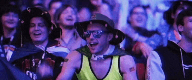 a man wearing sunglasses and a yellow tank top is sitting in a crowd of people ..