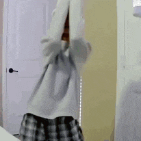 a man in a gray shirt and plaid shorts is standing in front of a door .