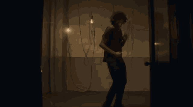 a man with dreadlocks is dancing in a dark room with wires hanging from the ceiling