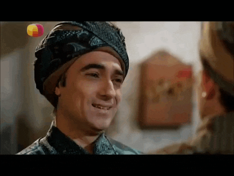 a man wearing a turban is smiling at another man in a room .