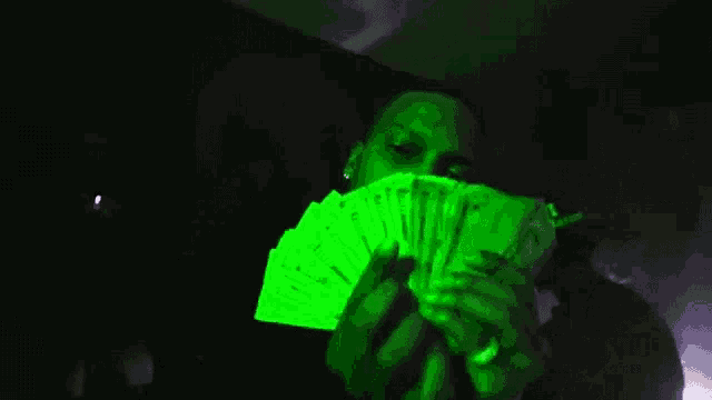 a man is holding a stack of money in his hands that is glowing in the dark .