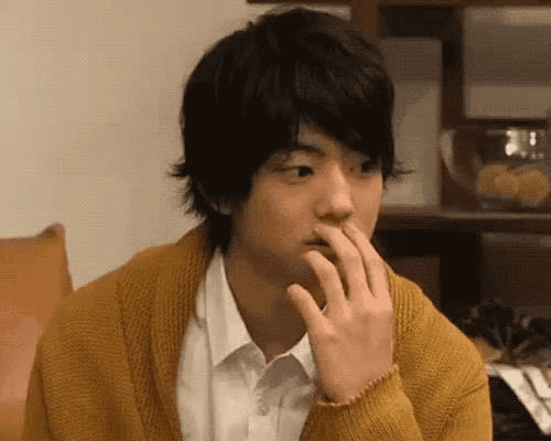 a young man wearing a yellow sweater and a white shirt is sitting on a couch .