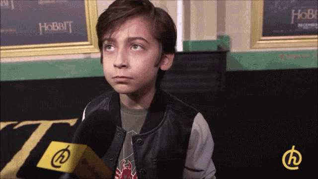 a young boy is talking into a microphone with a hobbit sign behind him