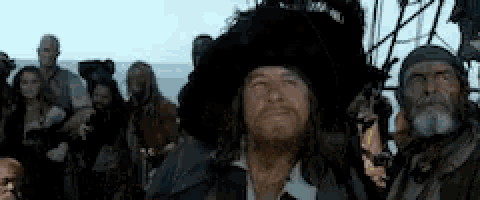 a man with a beard wearing a pirate hat is standing in front of a crowd of people .