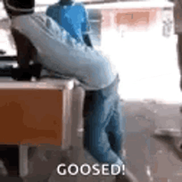 a man is sitting on a table with his legs crossed and the words `` goosed '' written on the ground .
