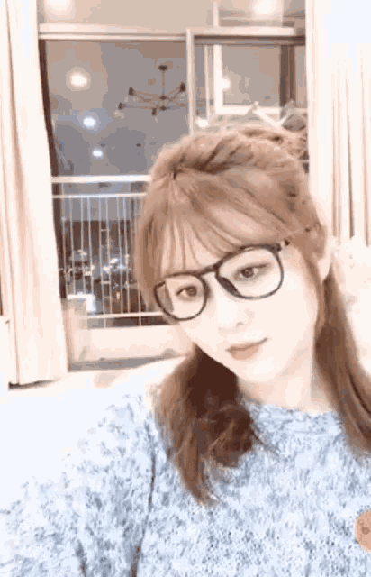 a woman wearing glasses and a blue sweater is standing in front of a window