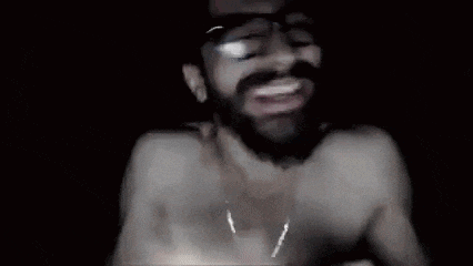 a man wearing sunglasses and a necklace is holding a cell phone in his hand in a dark room .