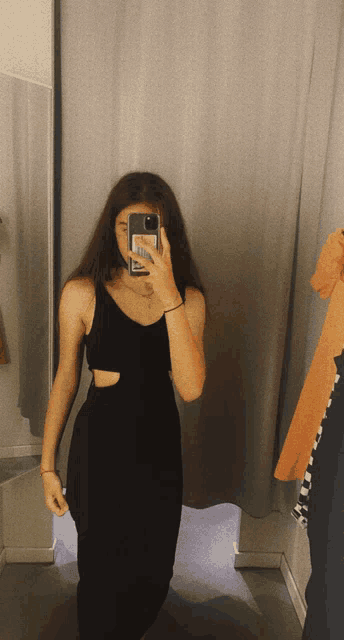 a woman in a black dress is taking a picture of herself in a dressing room