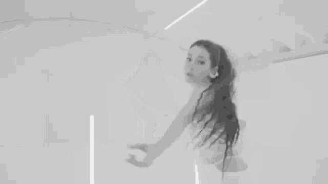 a woman with long hair in a ponytail is standing in a room with a rope around her neck .