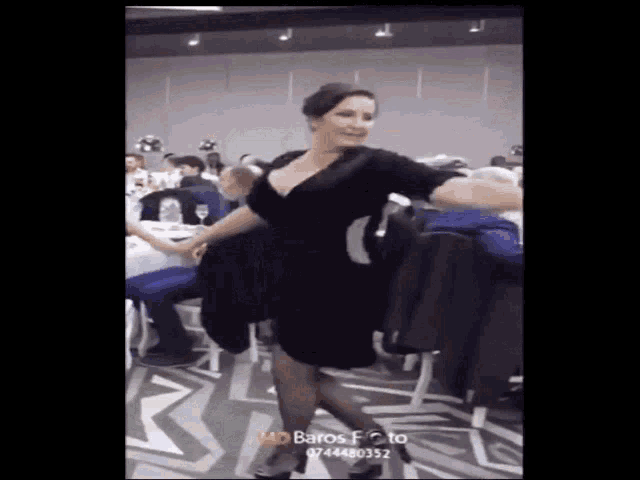 a woman in a black dress is dancing in front of a crowd