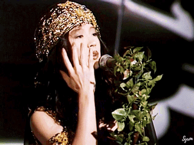 a woman is singing into a microphone while wearing a turban and holding a plant