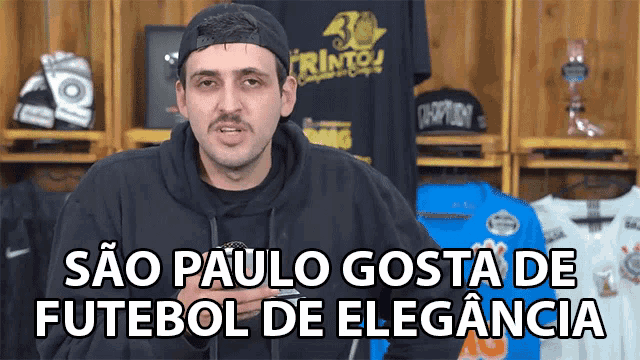 a man in a black hoodie stands in front of a sign that says sao paulo gosta de futbol de elegancia