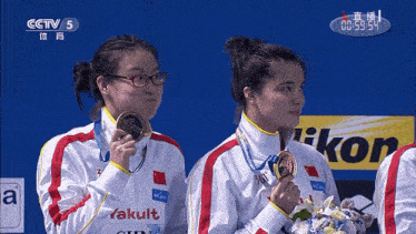 two female athletes holding medals in front of cctv 5