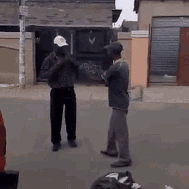 two men are standing on a street talking to each other in front of a building .