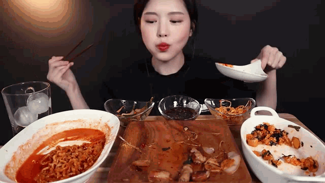 a woman is sitting at a table eating food with chopsticks and spoons