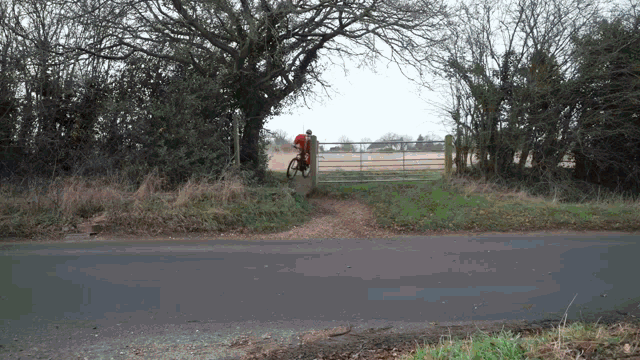 a man in a red shirt is riding a bike down a dirt road