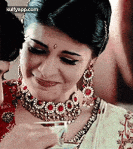 a woman in a necklace and earrings is smiling while holding a cup of tea .