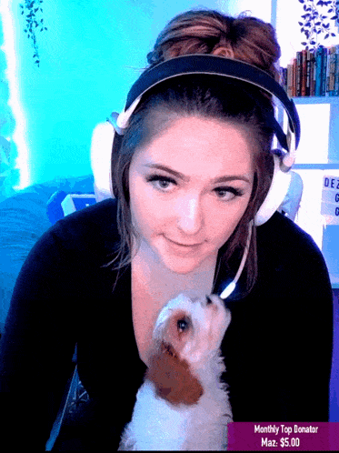 a woman wearing headphones and holding a small brown and white dog with a monthly top donator badge