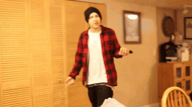 a man wearing a plaid shirt and a black beanie is dancing in a living room