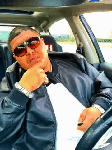 a man wearing sunglasses and a watch is sitting in the driver 's seat of a car