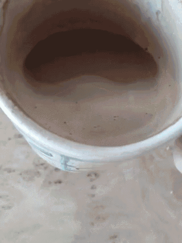 a close up of a cup of coffee on a table with a person holding it