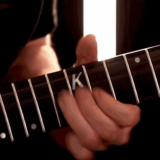 a close up of a person playing a guitar with the letter k on the neck