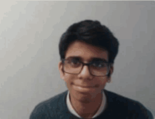a young man wearing glasses and a black sweater is smiling at the camera .