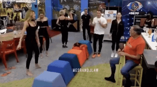 a group of people are dancing in a room with a man sitting in a chair
