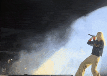 a woman singing into a microphone on a stage with smoke coming out of it