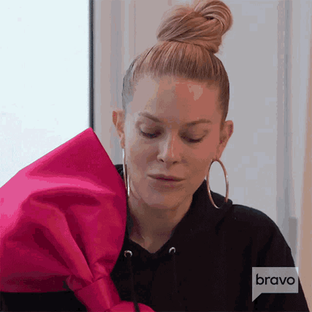 a woman wearing a black hoodie and hoop earrings is holding a pink bow in her hand .