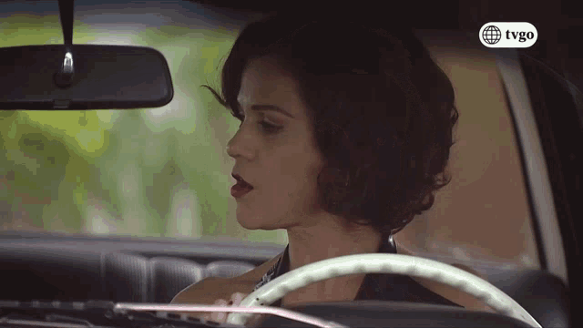 a woman sitting in a car with a tvgo logo on the bottom left
