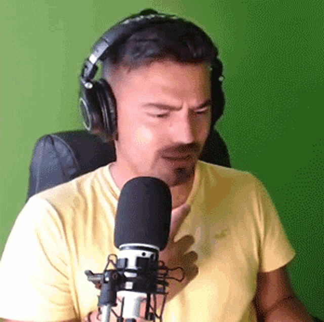 a man wearing headphones and a yellow shirt is holding a microphone .