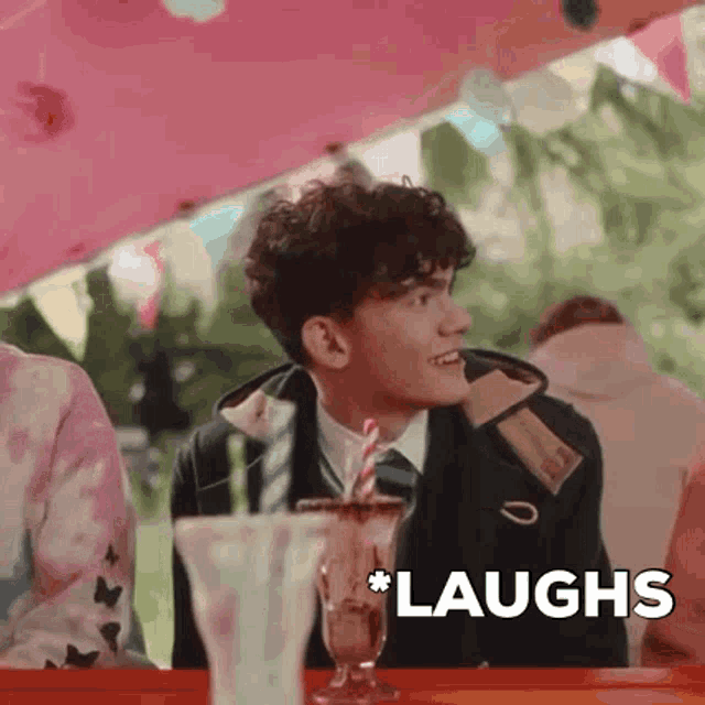 a young man is sitting at a table with a milkshake and the word laughs in the corner .