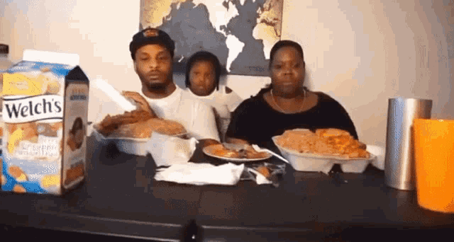 a family sits at a table with plates of food and a box of welch 's cornbread