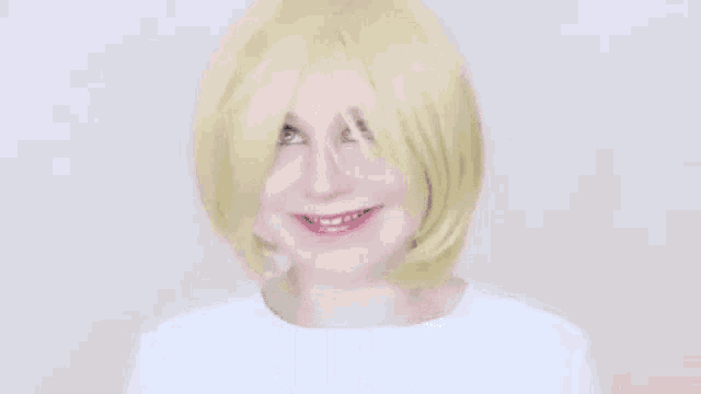 a woman wearing a blonde wig is making a funny face and smiling .