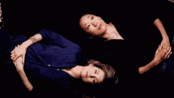two women are laying next to each other on a couch holding hands .