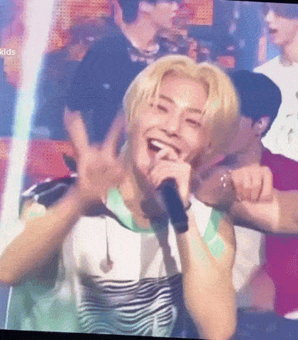 a man with blonde hair is singing into a microphone on a stage in front of a crowd .