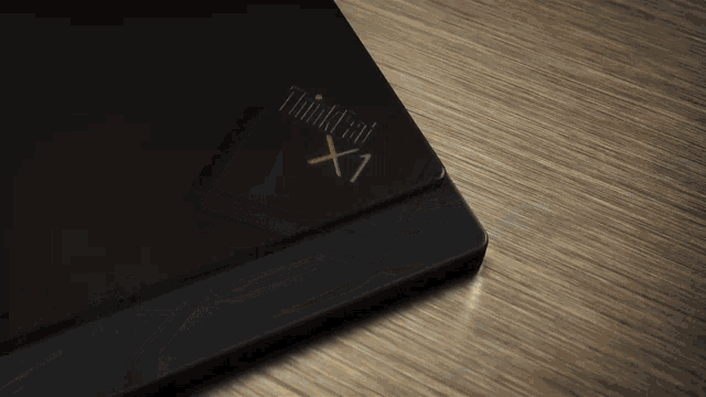 a black thinkpad x1 laptop is laying on a wooden table