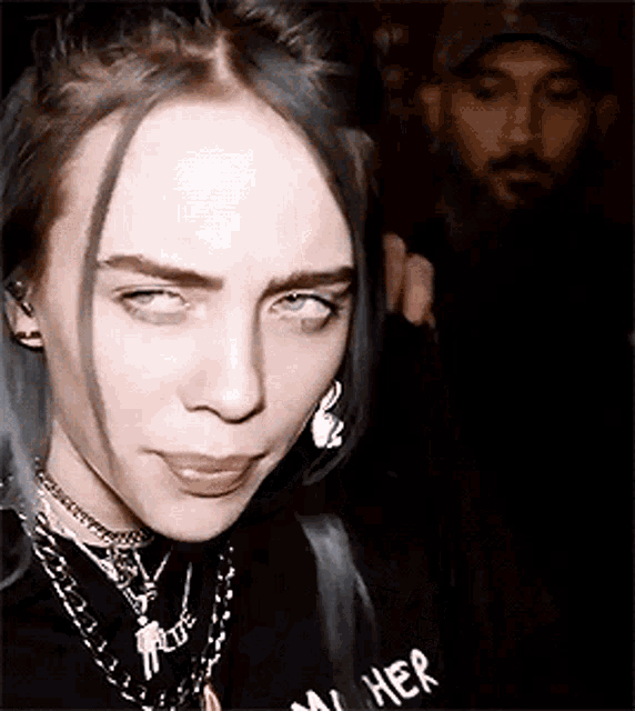 billie eilish is making a funny face while wearing a black shirt and necklaces .