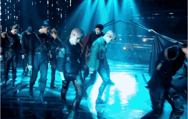 a group of people are dancing on a stage with blue lights