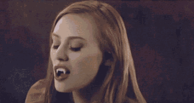 a woman with long red hair and vampire teeth is making a face .