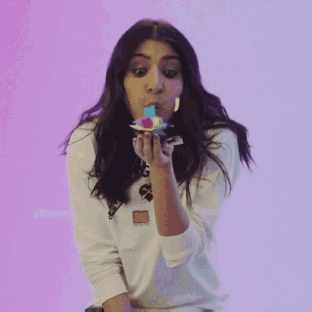 a woman blowing confetti in front of a pink background with the hashtag gkiberryman