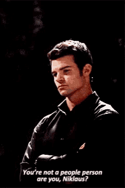 a man in a black shirt is standing with his arms crossed and is talking to someone .