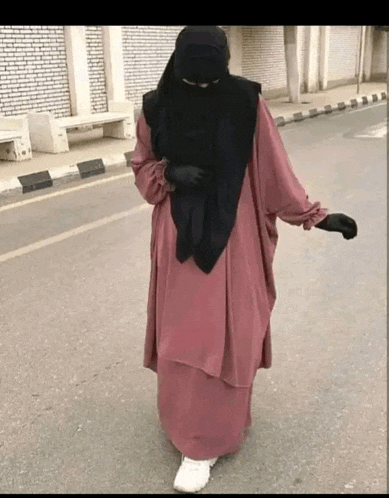a woman in a pink dress and black veil is walking down the street .
