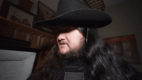 a man with long hair and a beard wearing a black hat