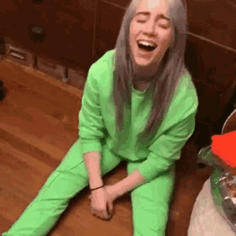 billie eilish is sitting on the floor with her mouth open and laughing .