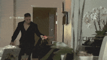 a man in a black suit is standing in front of a door with the watermark the maw